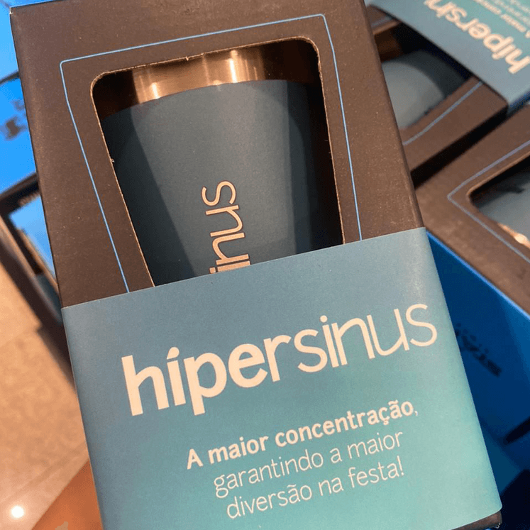 Fotografia 2 da ação de gifting criada pela VX Comunicação para a marca Hipersinus. A foto exibe um copo da marca Stanley, personalizado com a ID da marca Hipersinus, dentro de uma caixa preta. Envolvendo a caixa, uma tarja promocional com o texto: A maior concentração, garantindo a maior diversão na festa!