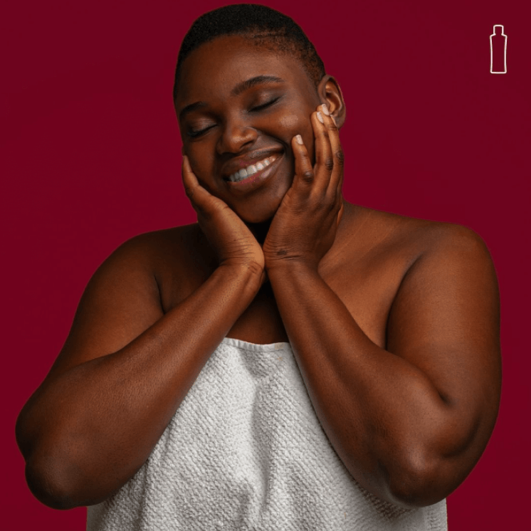 Fotografia de uma mulher negra sorrindo, com as mãos no rosto, em um fundo vermelho.