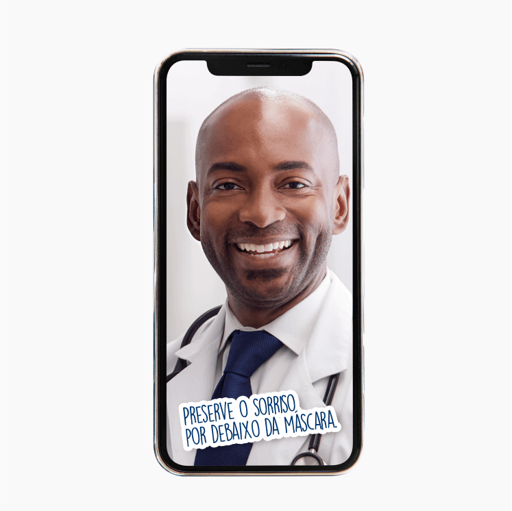Celular exibindo a fotografia de um homem de jaleco branco, sorrindo e olhando para a câmera. Abaixo, o texto: Preserve o sorriso por debaixo da máscara.