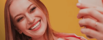 Peça publicitária desenvolvida pela VX Comunicação para a marca Sorriso Mode On, com uma mulher ruiva sorrindo para uma selfie no celular sobre um fundo laranja.